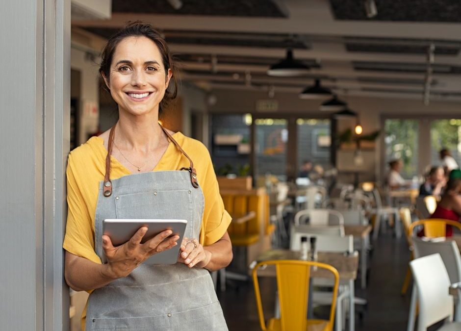 Alt tag: Small business owner wearing apron and holding a tablet inside a modern café or restaurant.