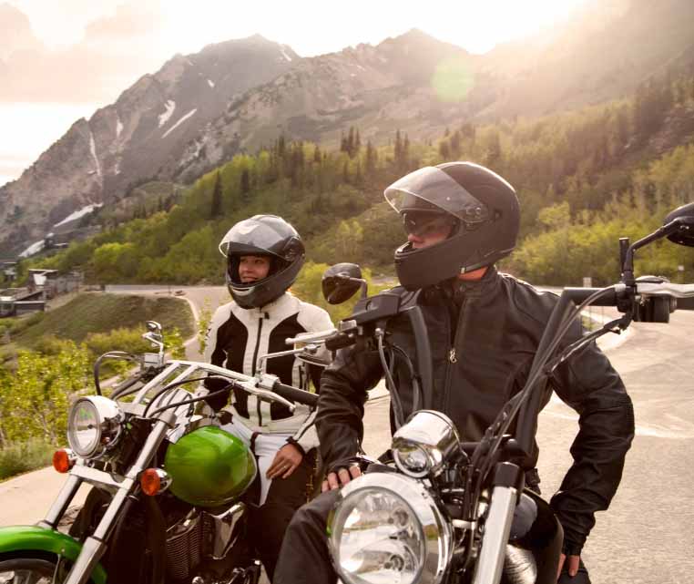 Two motorcyclists wearing helmets and protective jackets stopped on a mountain road