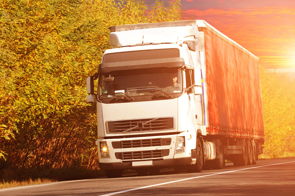 A truck drives along a road, surrounded by lush green trees in the background